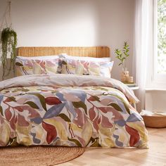 a bed with a colorful comforter on top of it next to a potted plant