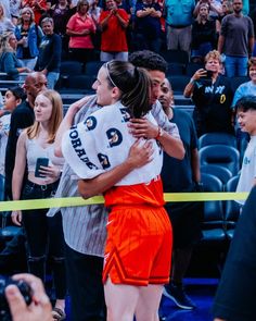 two girls hugging each other in front of a crowd at a basketball game with people watching