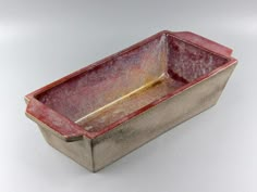 a red and gold rectangular dish sitting on a white surface with a silver rim around the edge