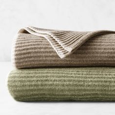 two blankets are folded on top of each other, one is green and the other is beige