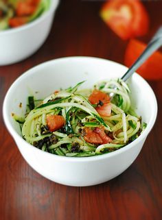 two bowls filled with zucchini noodles and vegetables on top of a wooden table