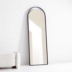 a mirror sitting on top of a white floor next to a chair and ottoman in front of a wall