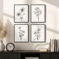 four black and white flowers are hanging on the wall next to a book shelf with books