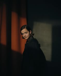 a woman standing in front of a curtain with her head turned to the side and looking at the camera