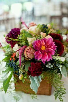 a wooden box filled with flowers and greenery on top of a white table cloth