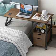 a laptop computer sitting on top of a wooden desk next to a bed with pillows