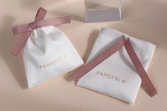 two small white bags with pink ribbons on them and a box containing the brand's logo