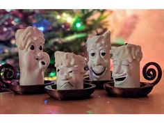 three ceramic heads with faces on them sitting in front of a christmas ornament