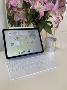 an open laptop computer sitting on top of a desk next to a vase with flowers