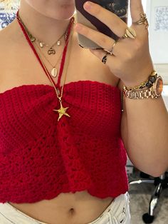 a woman taking a selfie while wearing a red crop top and white shorts with gold jewelry