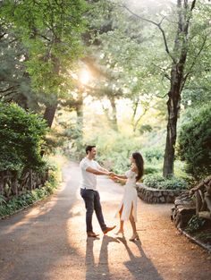 an engaged couple holding hands and standing in the middle of a road surrounded by trees