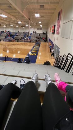 two people are sitting on the edge of a bench at a basketball court while others watch