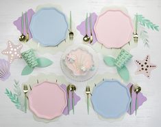 a table topped with plates and place settings covered in pastel blue, pink and green paper