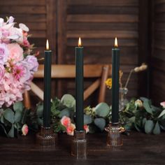 three candles sitting on top of a wooden table next to pink flowers and greenery