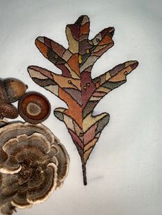 a close up of a piece of art with mushrooms and leaves on the bottom side