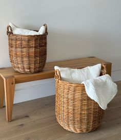 two wicker baskets sitting on top of a wooden bench next to a white wall