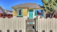 a small yellow house with a blue front door and white picket fence in front of it