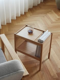 a small wooden table with magazines and a glass on it next to a chair in front of a window