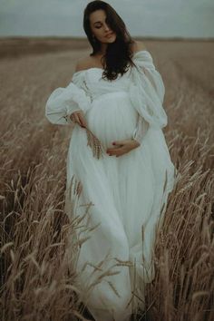 a pregnant woman in a white dress standing in a field