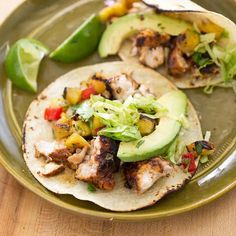 two tacos with chicken, lettuce and tomatoes on a plate next to lime wedges