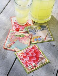 four square coasters with flowers on them next to a glass of lemonade and a drink