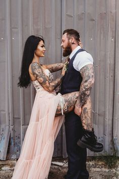 a tattooed man and woman standing next to each other in front of a metal wall