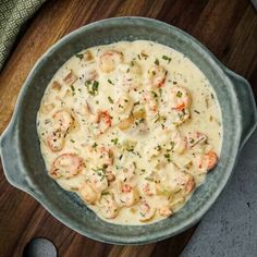 a bowl filled with shrimp and grits on top of a wooden table next to a spoon