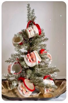 a small christmas tree with ornaments on it's branches and two mugs in the shape of santa claus