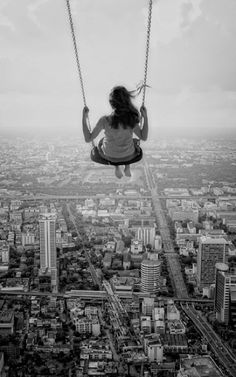 a woman sitting on a swing over a city