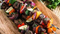 skewers of meat and vegetables on a wooden cutting board next to parsley