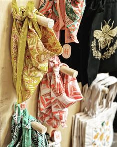 several different colored scarves hanging on a wall next to other scarves and purses