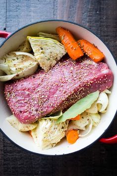 a pot filled with meat, cabbage and carrots on top of a wooden table