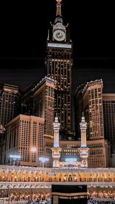 a large clock tower in the middle of a city with tall buildings behind it at night