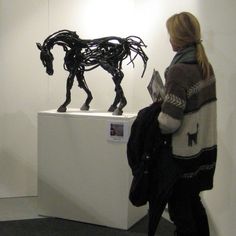 a woman standing next to a sculpture of a horse on display in a room with white walls