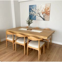 a dining room table with four chairs and a painting on the wall in the background