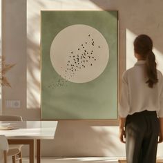 a woman standing in front of a painting with birds flying over her head on the wall