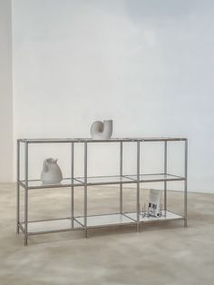 two white vases sitting on top of a metal shelf next to a magazine rack