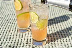 two glasses filled with lemonade and limes being poured into them