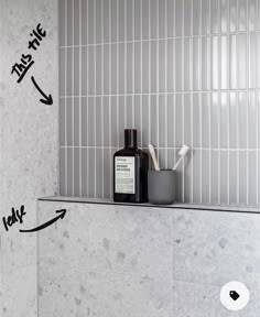 a bathroom with white tiled walls and gray tile on the wall, along with a black container filled with toothbrushes