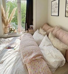 an unmade bed with many pillows and blankets on it in front of a window