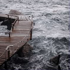 a wooden dock in the middle of some water with waves coming up on it and an umbrella