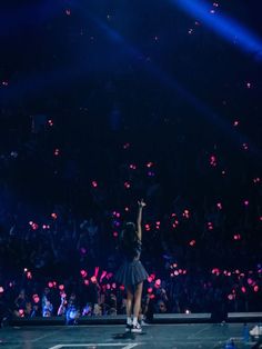 a person on a stage with their arms in the air and lights above her head