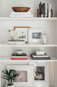 a white bookcase with books and pictures on it, along with a potted plant