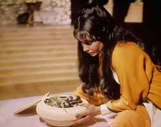 a woman sitting on the ground holding a bowl full of olives - stock image