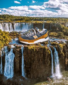 a pair of new balance shoes sitting on top of a cliff in front of a waterfall