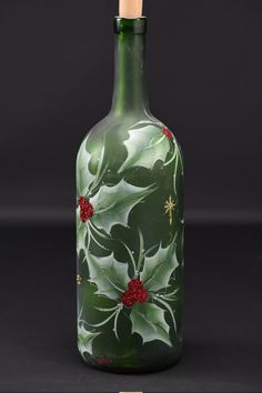 a green glass bottle with holly and red berries on the top is sitting in front of a black background