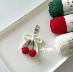 three balls of yarn and two crochet cherries on a white tray next to each other