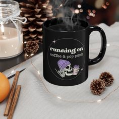 a black coffee mug sitting on top of a table next to candles and pine cones