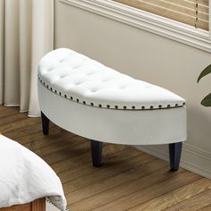 a white bench sitting on top of a hard wood floor next to a window with blinds