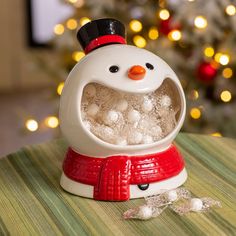 a snowman is sitting on a table next to a christmas tree